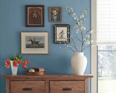 A table with vases in front of four prints hung on a wall painted Smoky Azurite.