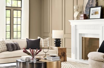 Una sala de estar grande y luminosa con paredes pintadas en SW 6150 Universal Khaki, una gran chimenea blanca y muebles beige.