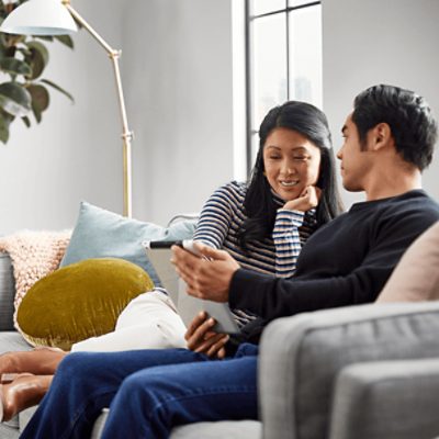 Two people sitting on a couch looking at a tablet together.