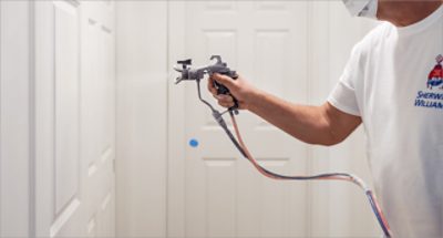 A person wearing a mask and applying paint to a wall with a spray gun.