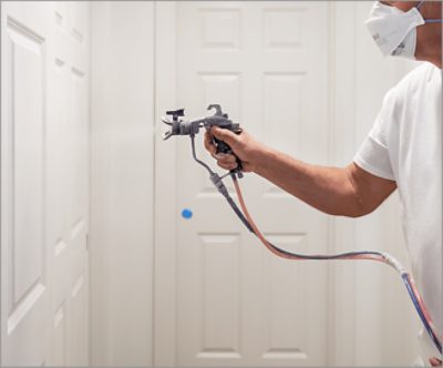 A person wearing a mask and applying paint to a wall with a spray gun.