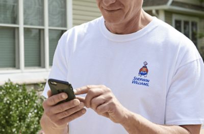 A person wearing a white t-shirt with the Sherwin-Williams logo using a smart phone.