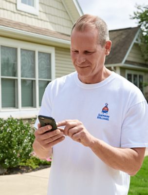 Person standing in front of a house with their mobile phone in their hand.