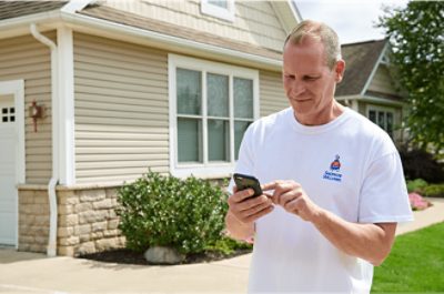 Person standing in front of a house with their mobile phone in their hand.