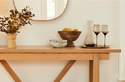 A stained table holding a carafe, two glasses and decor.