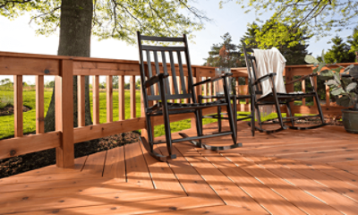 Two black wooden rocking chairs on a stained wood deck with a large field and trees behind.