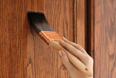 A person staining a piece of furniture with a brush.
