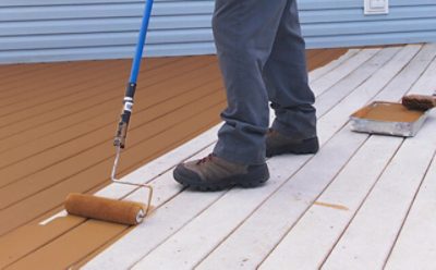 A person using a roller brush to paint a deck.