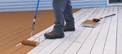 A man staining a deck with a paint roller.