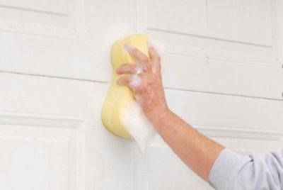 Prepping a garage door to paint by washing with a sponge.