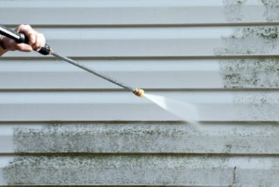 A person using a power washer to clean the side of a house.