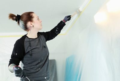 A person cutting in with a brush on a ceiling.