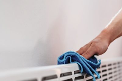 Wiping down a baseboard heater with a cloth.