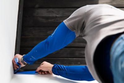 A person using blue masking tape to protect the edges from paint.