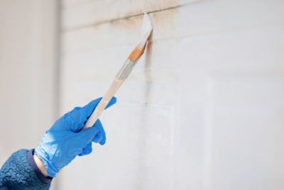 A person wearing a latex glove while painting a garage door with a brush.