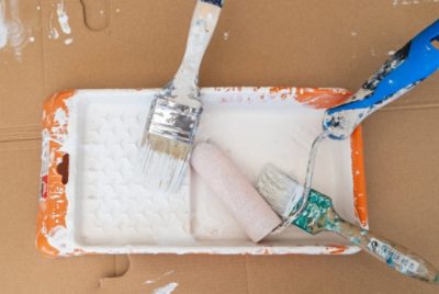 Used brushes and a roller in a paint tray with white paint.