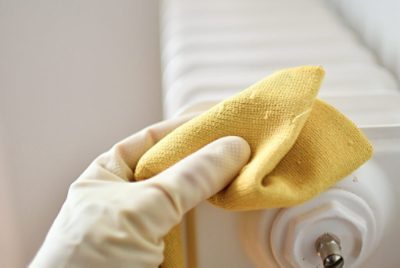 Wiping a radiator with a cloth while wearing rubber gloves.