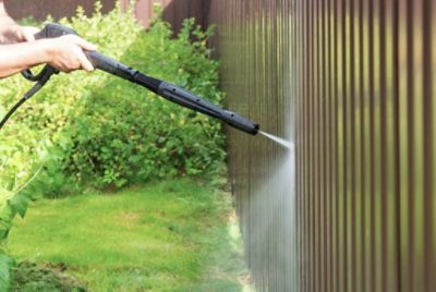 A person power washing a wood fence.