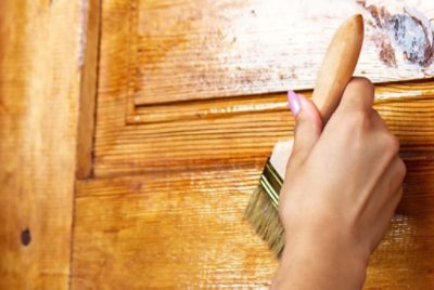 A person applying stain to a cabinet with a brush.