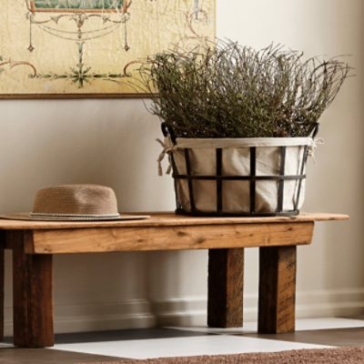 A bench in an entry way holding a hat and a large basket of tall dried decorative grass.