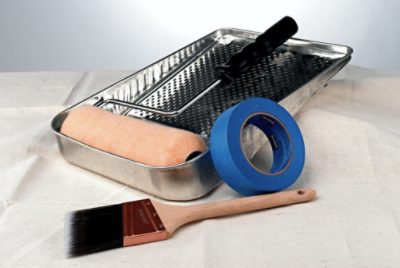 A clean paint brush, roller, tray and tape on a drop cloth.