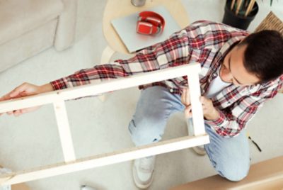A person looking at a piece of wood furniture by holding it up to eye level.