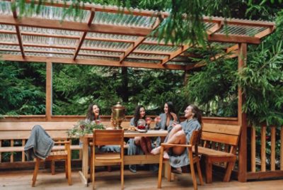 A group of people sitting under a stained pergola surrounded by lush green evergreen trees.