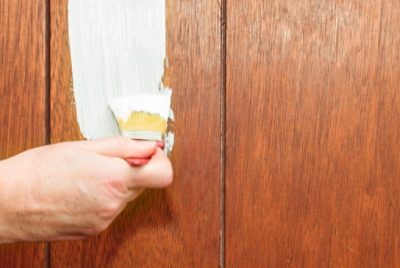 A person brushing paint onto wood paneling.