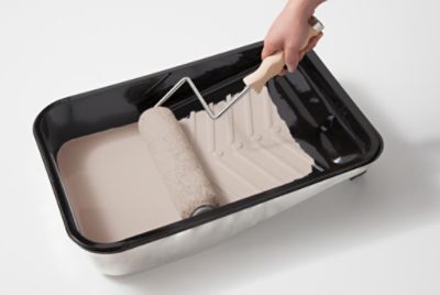 A person using a roller in a paint tray.