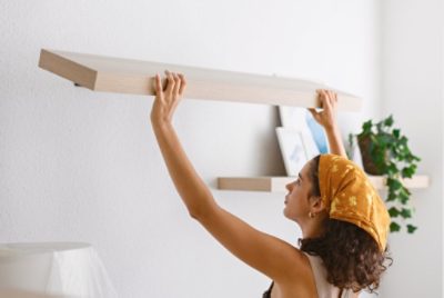 A person hanging a long floating shelf on a wall.