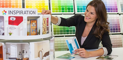 A woman in a dark blazer in front of a color chips wall selecting postcards from a rotating display.
