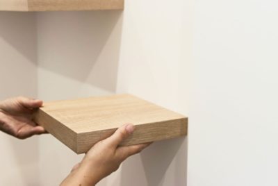 A person holding a floating shelf up to a wall.