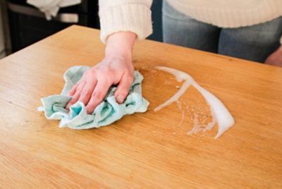 Close-up of a person using a cloth to clean the surface of a wooden table.
