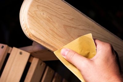 Close-up of a person sanding the arm of a wooden chair using sandpaper.