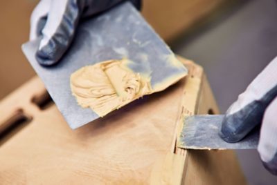 Close-up of a person wearing gloves while applying wood filler to a wooden surface.