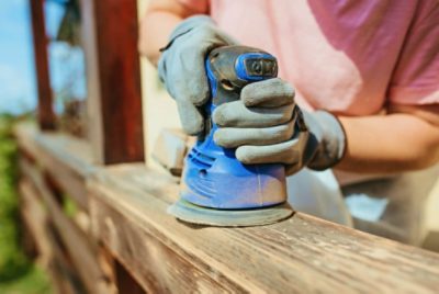 Using an electric sander on a stained wood deck railing.