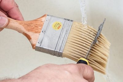 A person cleaning a paint brush by rinsing it under water.