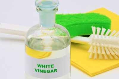 A green sponge and cleaning brush next to a bottle of white vinegar.