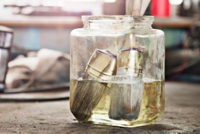 Two paint brushes sitting in water inside a glass container. 