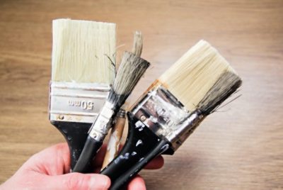 A person holding various paint brush sizes that are both un-used and used. 