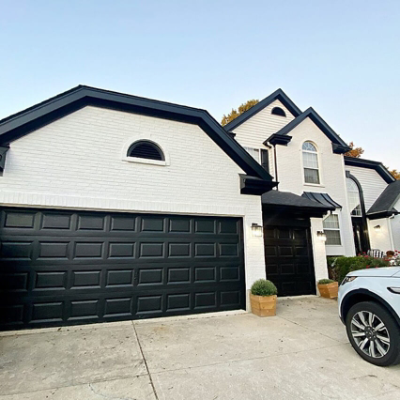 White brick home with black garage doors, gutters and roof.