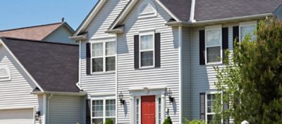 A large suburban home with neutral color vinyl siding and manicured landscaping.