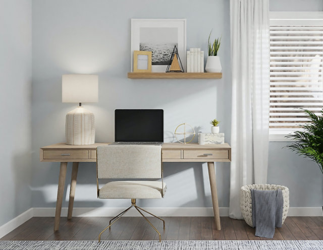 Light wood desk with modern chair in a bright home office, accented by white curtains and a green plant.
