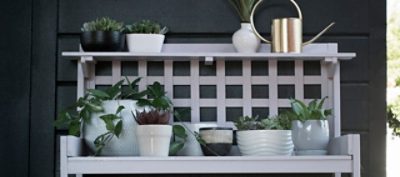 Several flower pots on top of a purple flower stand in front of a dark wall.