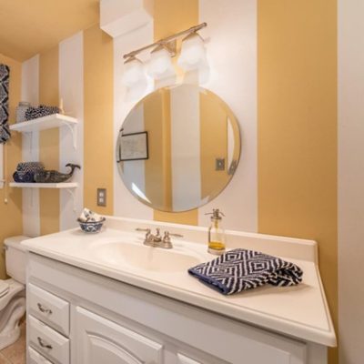 A bathroom vanity with vertical white and yellow stripes on the wall. S-W featured color: SW 6128 Blonde