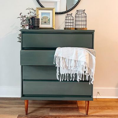 A dark green dresser with a white blanket draped over a drawer. S-W colors featured: SW 6188 Shade Grown.
