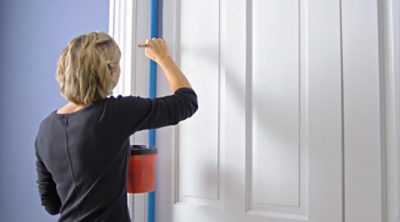 A woman painting the edges of a door in a room. SW color featured: SW 6243 Distance.