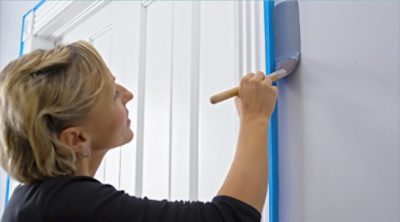 A woman painting wall edges in a room. SW color featured: SW 6243 Distance.