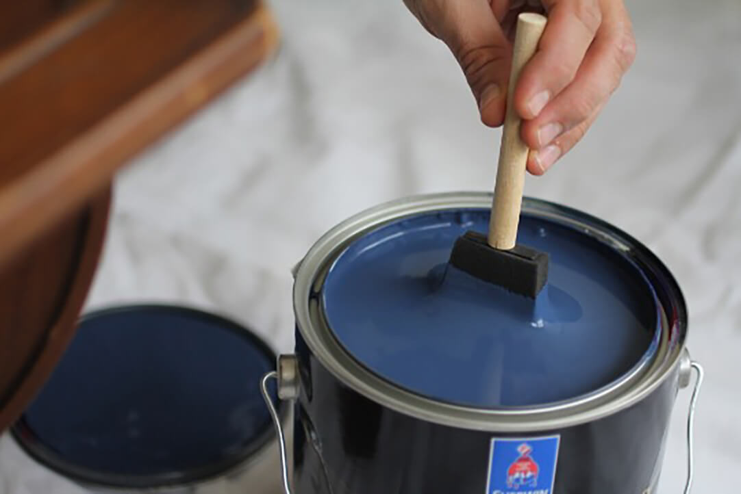 A sponge brush being dipped in navy blue paint. S-W color featured: SW 6244 Naval.