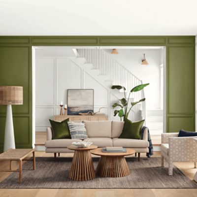 A living room with neutral colored furniture and walls painted with SW 6246 Basque Green that leads into an all white entryway with a large staircase.